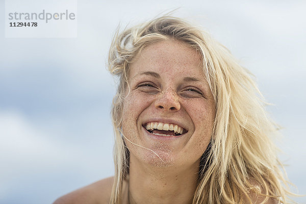 Porträt einer glücklichen jungen Frau mit Sand im Gesicht