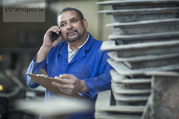 Mann mit Klemmbrett am Telefon in einer Fabrik