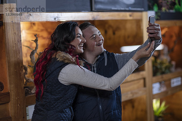 Junger Mann mit Down-Syndrom und junge Frau  die einen Selfie auf der Reptilienausstellung nimmt.
