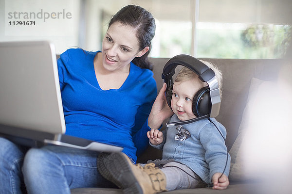Mutter mit Kleinkind mit Kopfhörer und Laptop zu Hause
