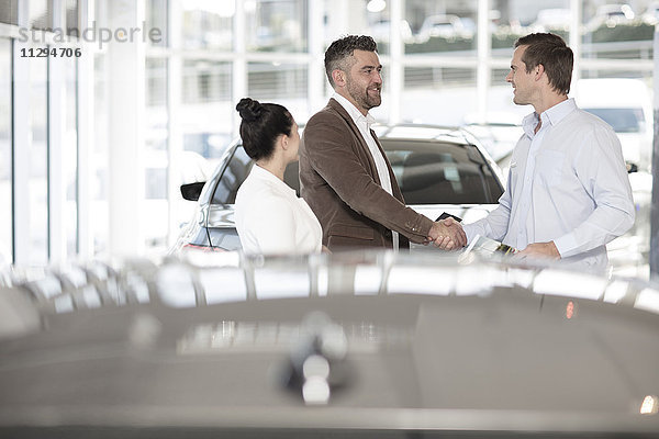 Autohändler schüttelt dem Mann im Autohaus die Hand