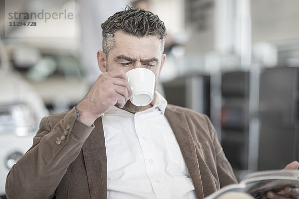 Mann beim Kaffeetrinken Lesemagazin im Autohaus