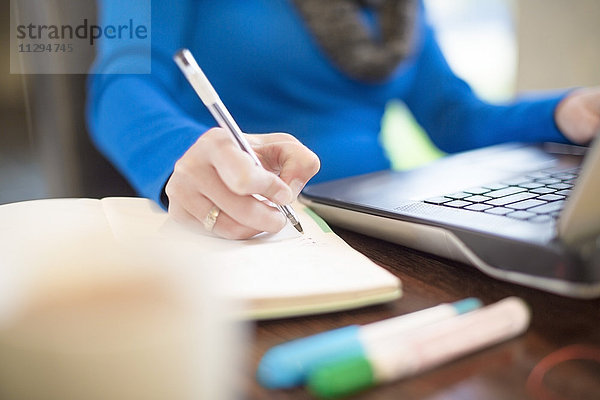 Frau am Schreibtisch mit Laptop-Schriftzug im Notebook