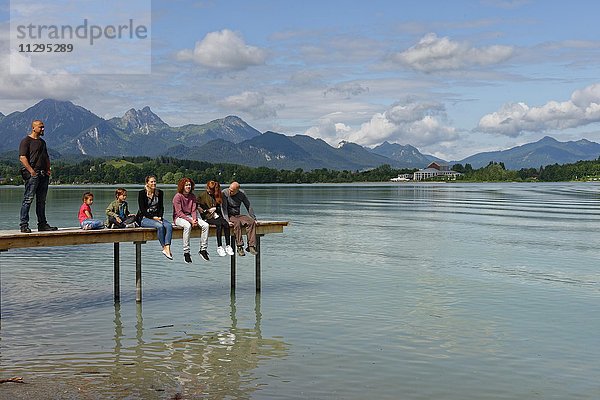 Familie mit Kindern sitzen auf einem Steg am Forggensee  bei Füssen  Allgäu  Bayern  Deutschland  Europa