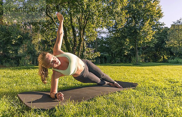 Planks auf der Seite  Junge Frau in Sportkleidung trainiert auf einer Matte in der Wiese in einem Park  München  Oberbayern  Bayern  Deutschland  Europa