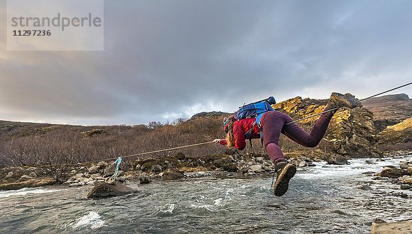 Junge Frau überquert den Fluss Botnsá  mit Seil zur Flussüberquerung  Hvalfjarðarsveit  Vesturland  Island  Europa