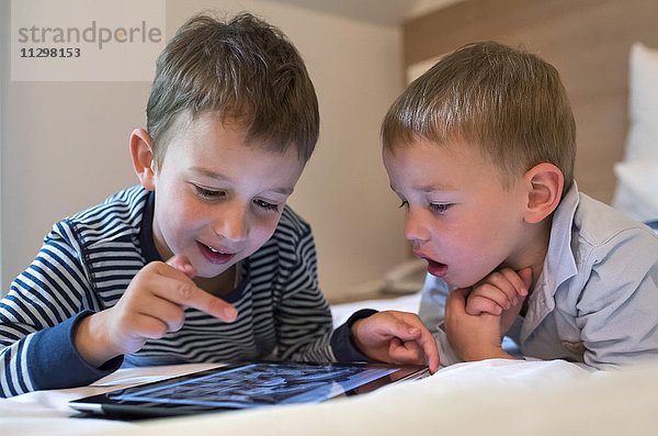 Zwei Jungen  Geschwister liegen auf einem Bett und spielen mit einem iPad  Tablet PC