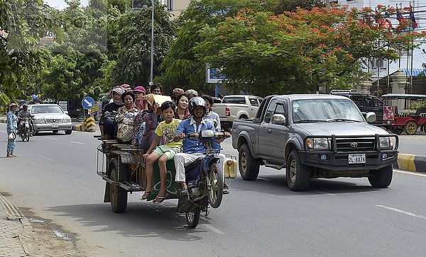 Mann auf Motorroller macht eine Wheelie  mit Menschen beladener Anhänger  Phnom Penh  Kambodscha  Asien