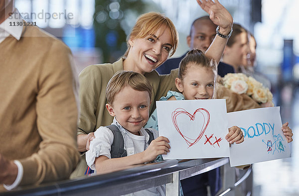 Mutter und Kinder mit Begrüßungsschildern für Vater am Flughafen