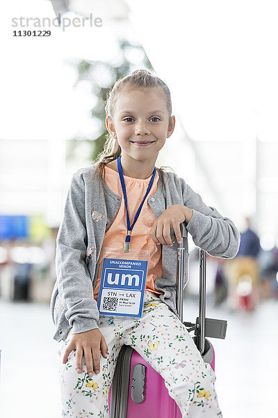 Portrait lächelndes Mädchen sitzend auf Koffer im Flughafen