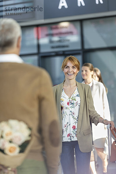 Ehemann überrascht Frau mit Blumen am Flughafen