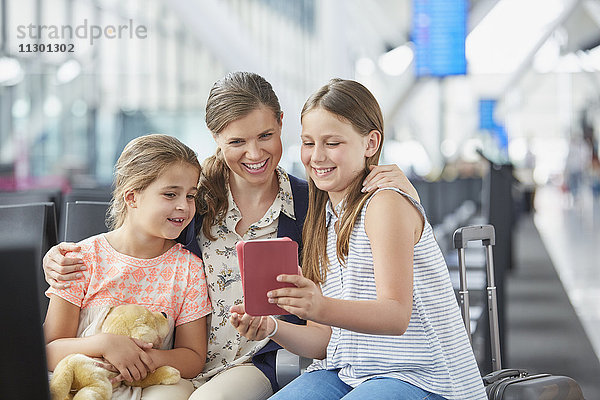 Mutter und Töchter mit digitalem Tablett im Abflugbereich des Flughafens