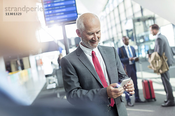 Geschäftsmann SMS mit Handy in der Flughafenhalle