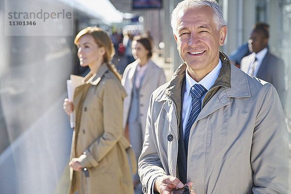 Porträt eines lächelnden Geschäftsmannes auf dem sonnigen Bahnsteig des Bahnhofs