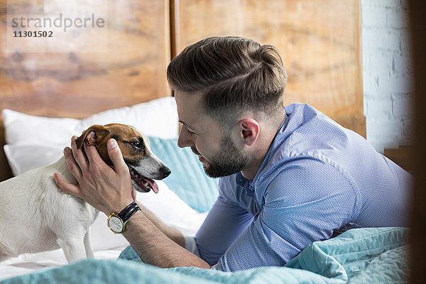 Mann streichelt Jack Russell Terrier auf dem Bett