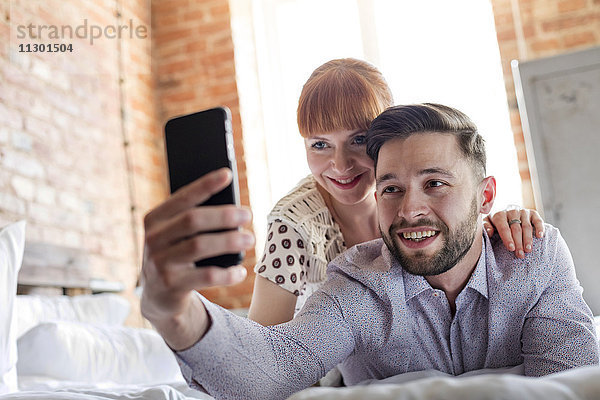 Paar  das auf dem Bett liegt und Selfie mit Fotohandy nimmt