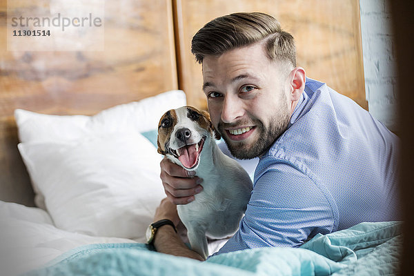 Portrait lächelnder Mann streichelt Jack Russell Terrier Hund im Bett