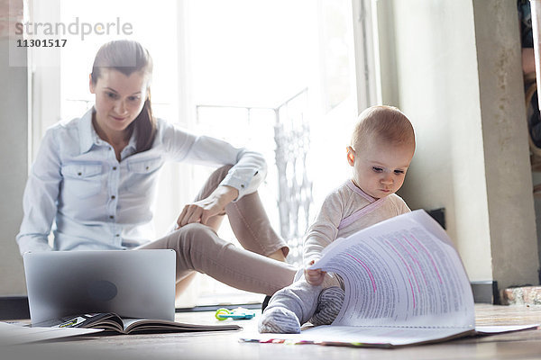 Neugierige kleine Tochter  die sich den Papierkram neben der Mutter anschaut  die am Laptop arbeitet.
