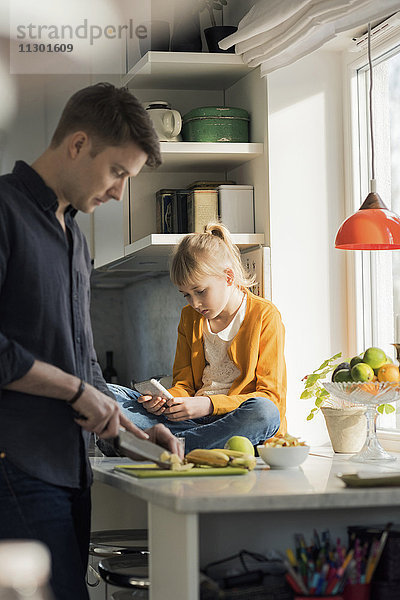 Vater schneidet Früchte weißes Mädchen mit dem Handy in der Küche