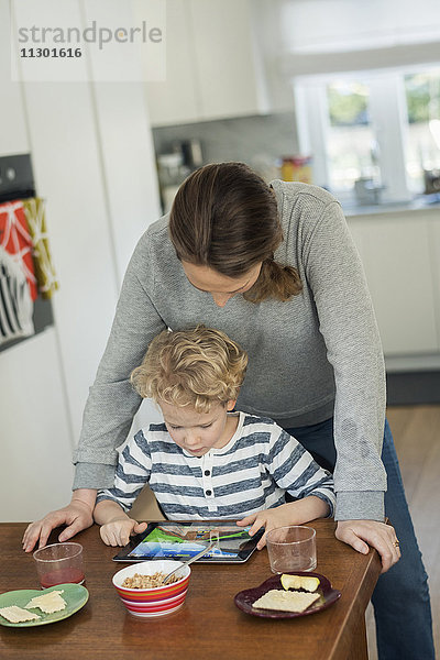 Mutter und Sohn mit digitalem Tablett am Esstisch im Wohnzimmer
