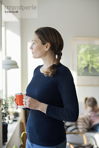 Frau stehend mit Kaffeetasse im Wohnzimmer zu Hause