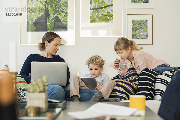 Mutter und Kinder nutzen Technologien auf dem Sofa zu Hause