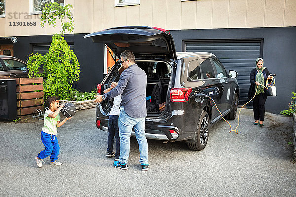 Vater spielt mit Kindern  während die Mutter das elektrische Ladegerät mit dem Auto rollt.