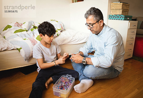 Vater und Sohn spielen mit Gummibändern  während sie zu Hause auf dem Parkettboden sitzen.