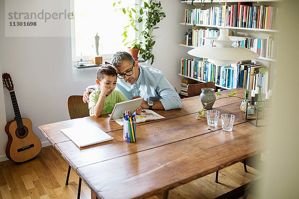 Vater und Sohn mit digitalem Tablett am Tisch