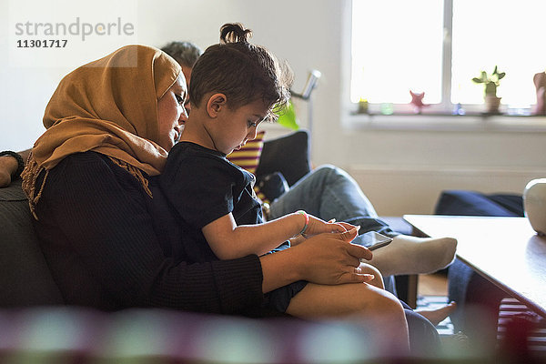 Seitenansicht von Mutter und Sohn beim Sitzen auf dem Sofa zu Hause mit digitalem Tablett