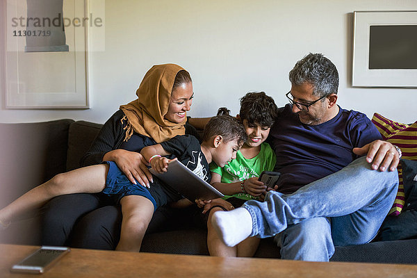 Verspielte Familie mit Smartphone im Sitzen auf dem Sofa zu Hause