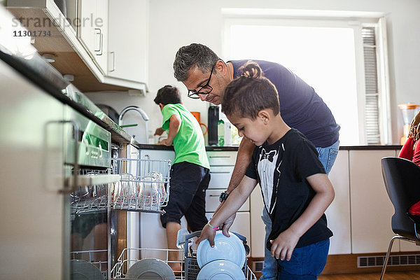 Vater und Sohn arrangieren Teller in der Spülmaschine in der Küche