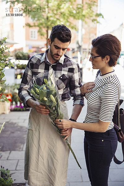 Weibliche Kundin kauft Blumen vom männlichen Besitzer auf dem Bürgersteig