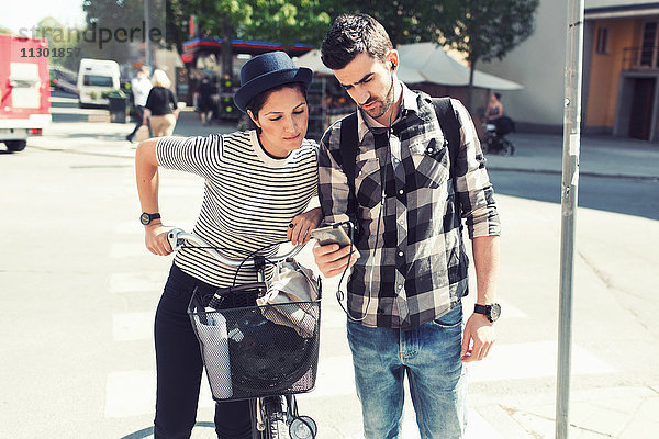 Paar mit Smartphone im Stehen mit dem Fahrrad auf der Straße