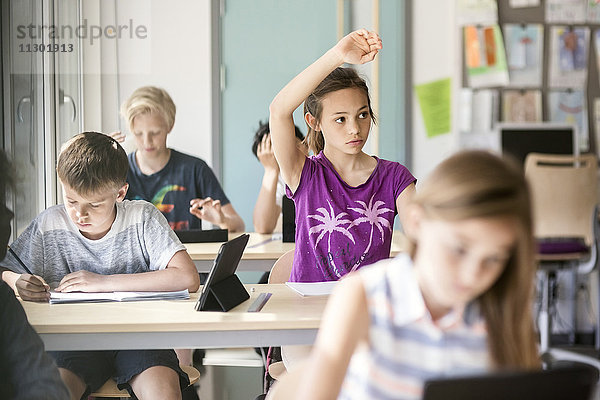 Schülerin hebt Hand am Schreibtisch im Klassenzimmer