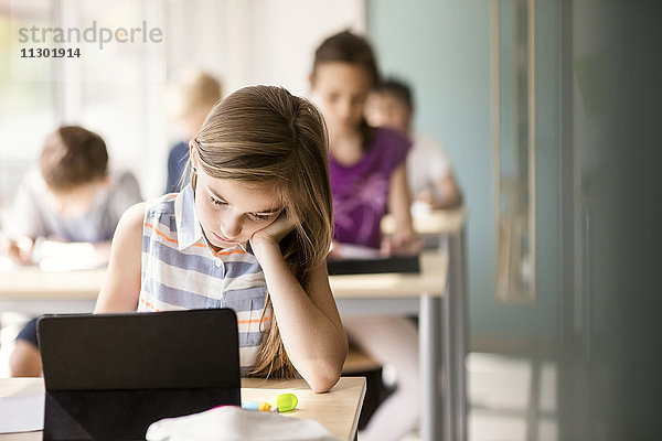 Schülerin am Schreibtisch mit Schülern im Klassenzimmer