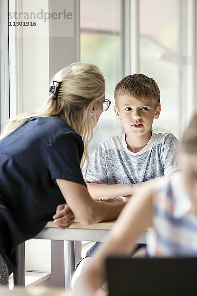 Lehrer assistierender Junge am Schreibtisch mit Mädchen im Vordergrund