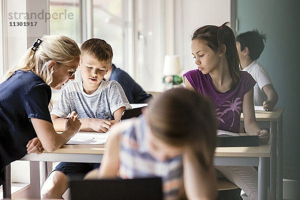 Lehrer assistiert Schulkindern am Schreibtisch im Klassenzimmer