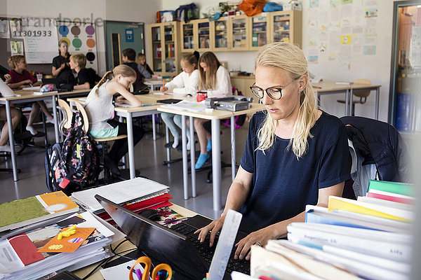 Lehrer mit Laptop auf dem Schreibtisch mit Schülern im Klassenzimmer