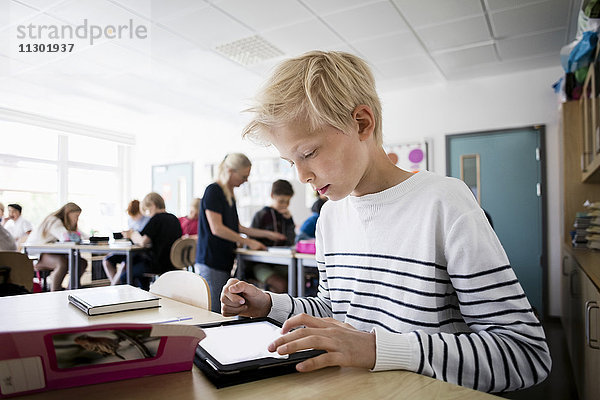 Junge mit Tablet PC am Schreibtisch im Klassenzimmer