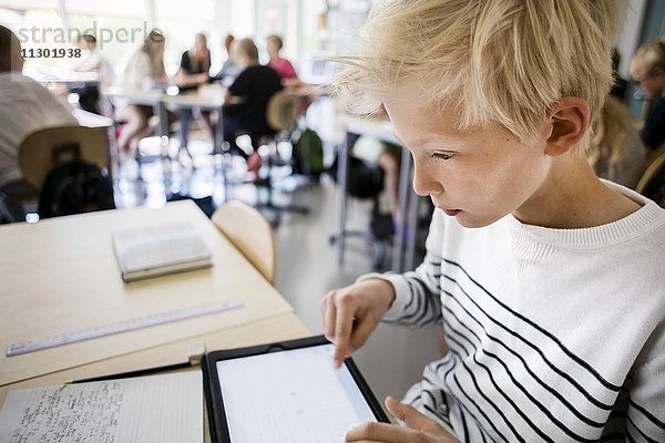 Junge mit digitalem Tablett am Schreibtisch im Klassenzimmer