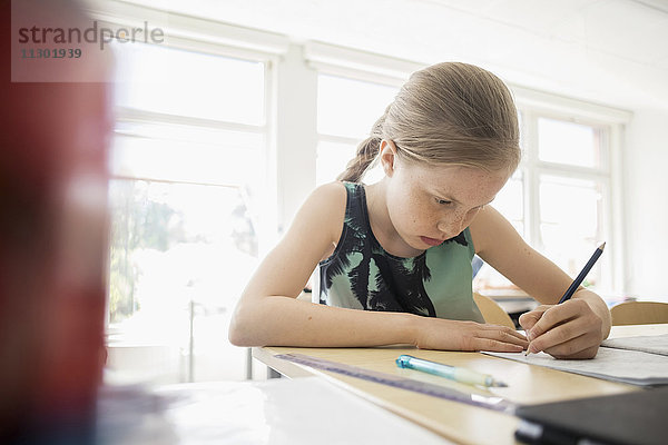 Mädchen schreiben in Buch gegen Fenster im Klassenzimmer