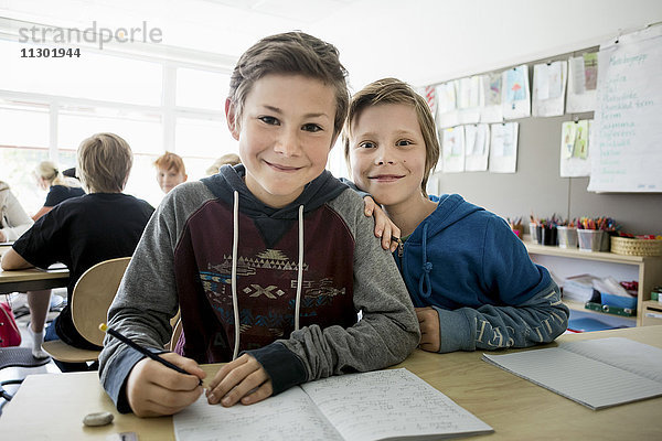 Porträt von glücklichen Jungen mit Büchern auf dem Schreibtisch im Klassenzimmer