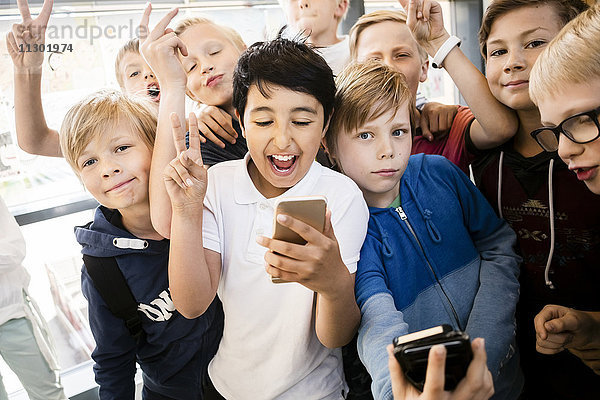 Fröhliche Schulkinder mit Handy und Friedensschild im Flur