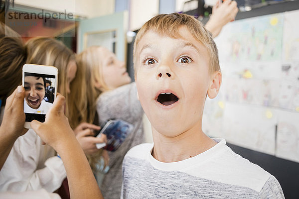 Überraschter Junge steht inmitten von Freunden  die Selfie auf dem Flur nehmen.