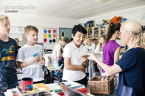 Lehrer  der dem Schüler im Klassenzimmer ein Handy gibt