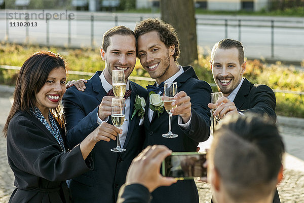 Fröhliche Freunde mit Champagnerflöten beim Fotografieren während der Hochzeitszeremonie