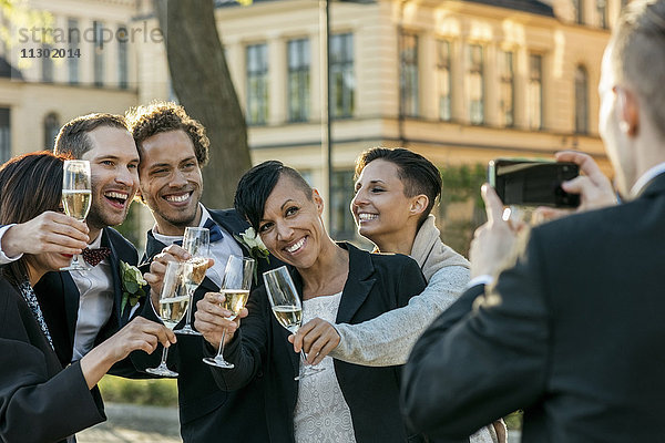 Rückansicht eines Mannes  der Freunde mit Champagnerflöten fotografiert.