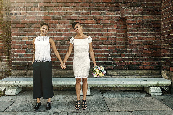 Glückliches jungvermähltes lesbisches Paar steht an der Ziegelmauer