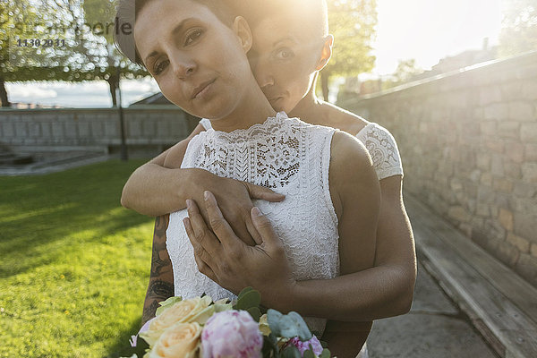Porträt eines selbstbewussten jungvermählten lesbischen Paares mit Blumenstrauß im Park